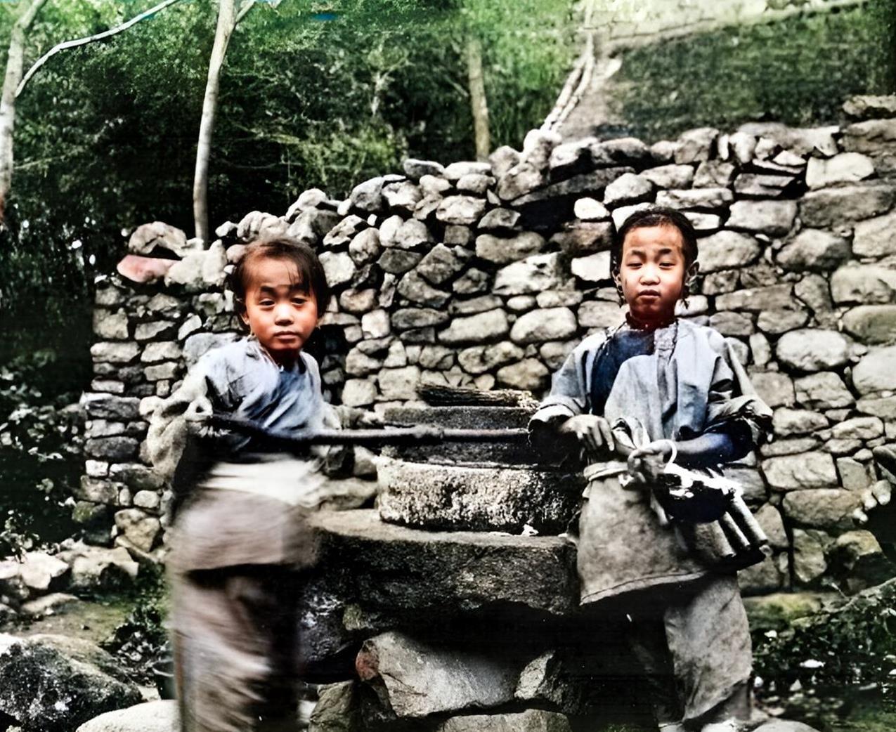 1906年，青岛两名漂亮的小姑娘在墙外推磨。由于年龄小，力气小，姐妹俩中任何一人
