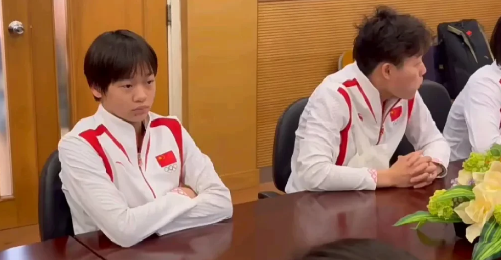 奥运三冠王，归来仍是少年！全红婵坐着从桌子上的果盘拿了一个葡萄吃了，旁边穿西服看