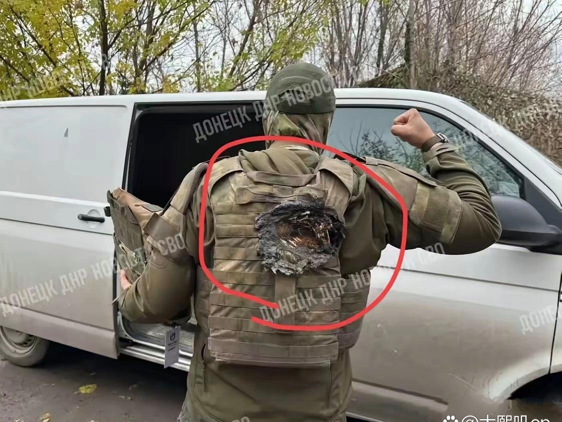 一名被防弹衣救了的士兵向队友展示自己的后背，由于身穿了内置陶瓷插板的防弹护具，这