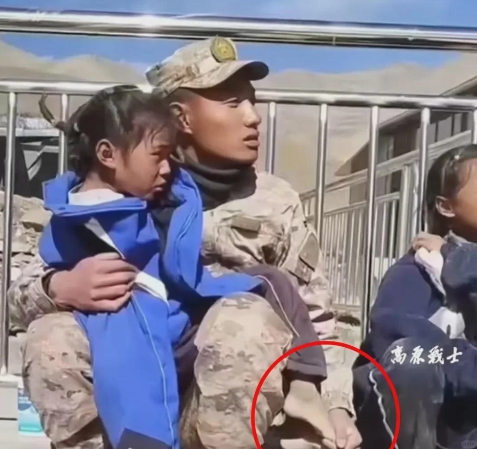 震区救援现场，一个救援士兵坐在路边，怀里抱着一个被救出来的小女孩。小女孩的脚是光