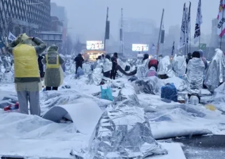 数千韩国民众在大雪中身披保温毯坚持集会。室外大批人群冒着严寒，迎着大雪。室内尹锡