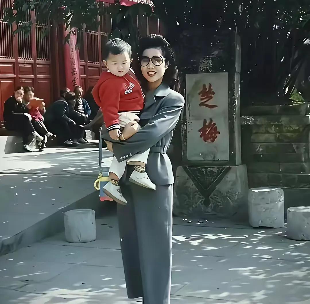 这是当年梦鸽老师抱着李天一在游玩时的留影，穿着打扮上很朴素，手里还拎着个小孩水壶