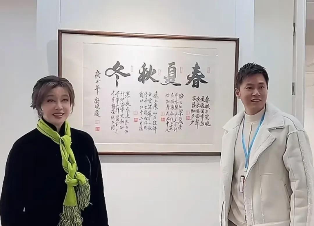 刘晓庆的书画作品参加展览，与经纪人易纲在作品前合影！
庆姐黑色中式搭配绿色围巾，
