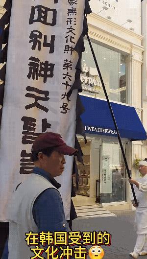 韩国街头民俗活动，前面打着幡，后边的人是白衣、白裤、白鞋子、头上还带着白带子，以