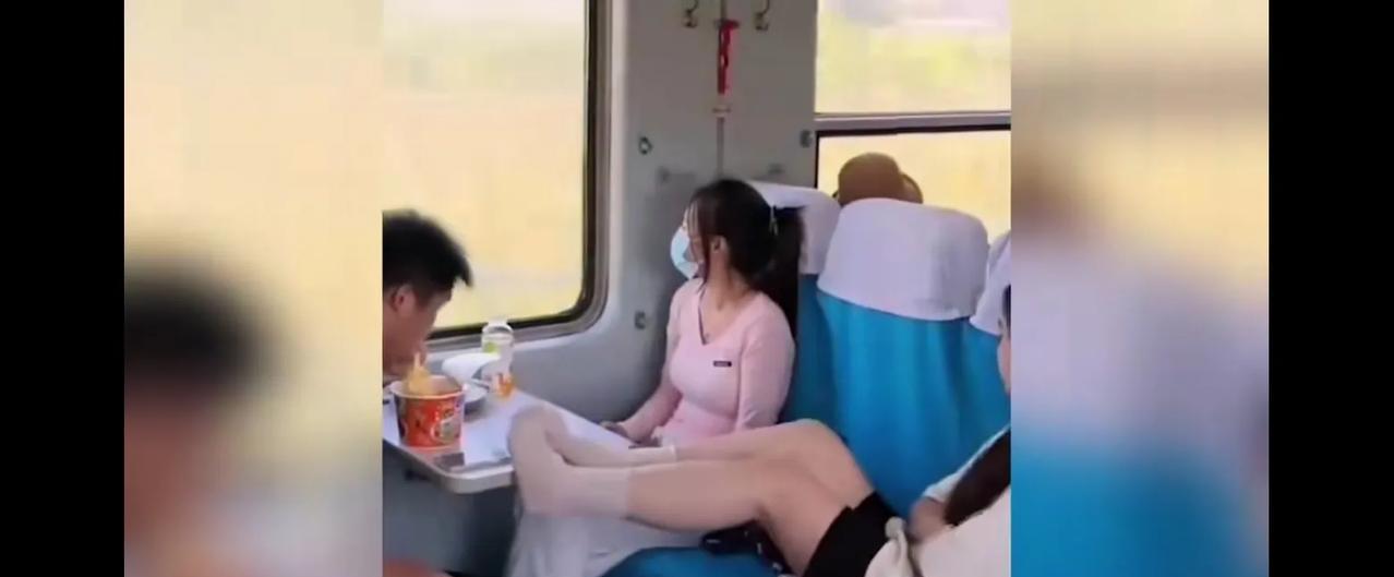 一男子在列车上吃桶面，期间一女子脱了鞋把脚伸到餐板上，离着男子的桶面没有半尺远，