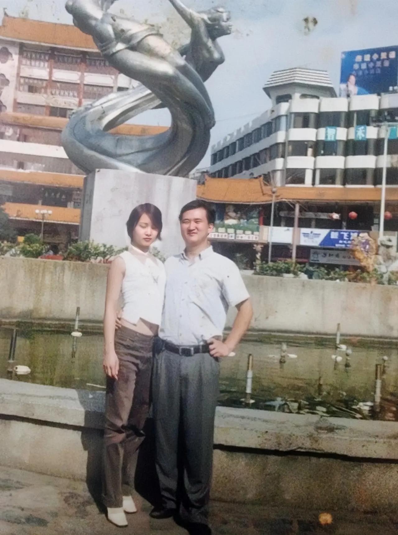 20多年前贵州兴义，有一对年轻夫妻在街心花园喷水池前留影，姑娘的打扮很潮。 小伙