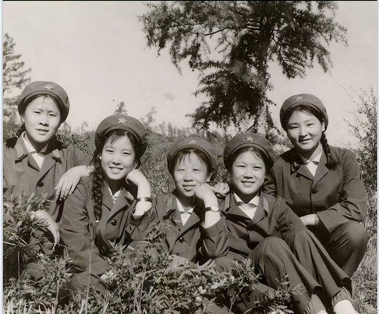 这是六十年代五位女战士在山坡草地上合影。她们梳着长长的麻花辫，戴的帽子中间有一颗