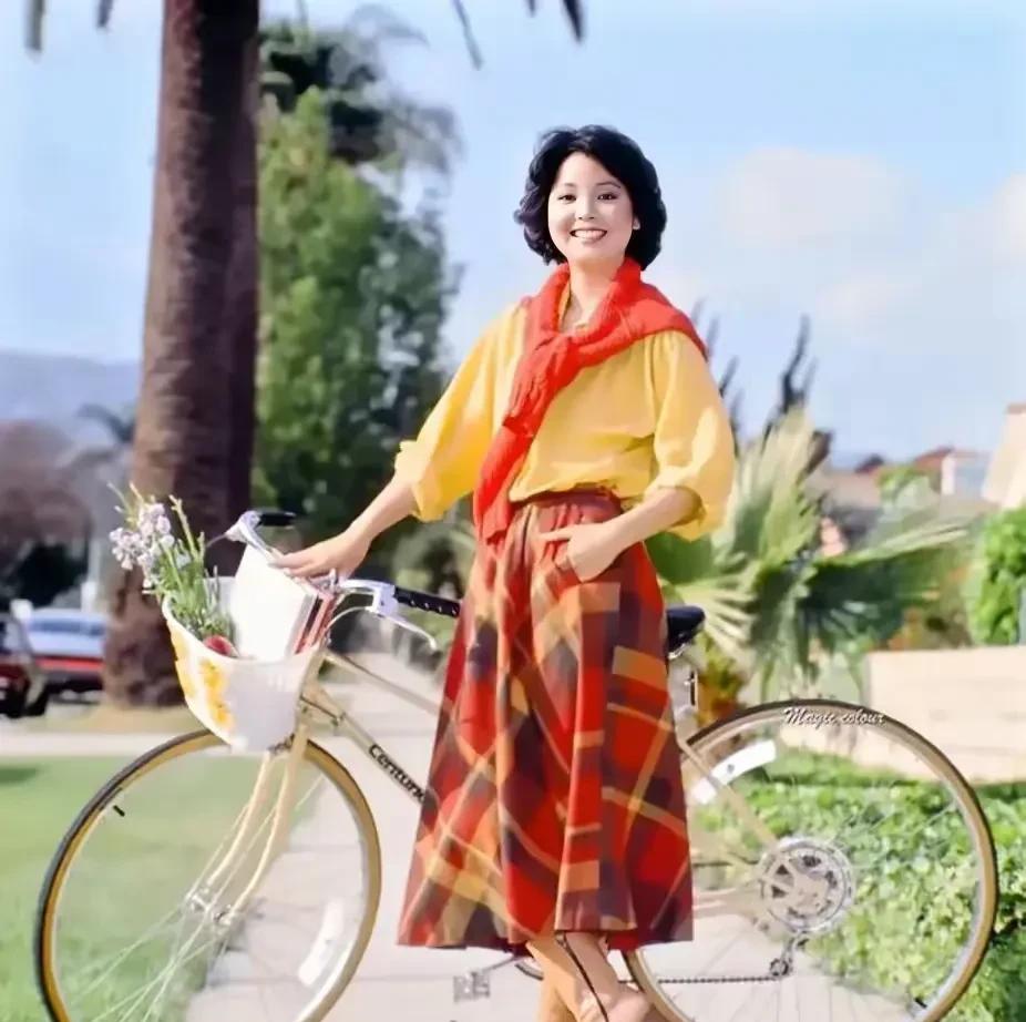 一张摄于1980年美国加州的老照片，画面中，邓丽君轻推着自行车，步伐悠然。她的面