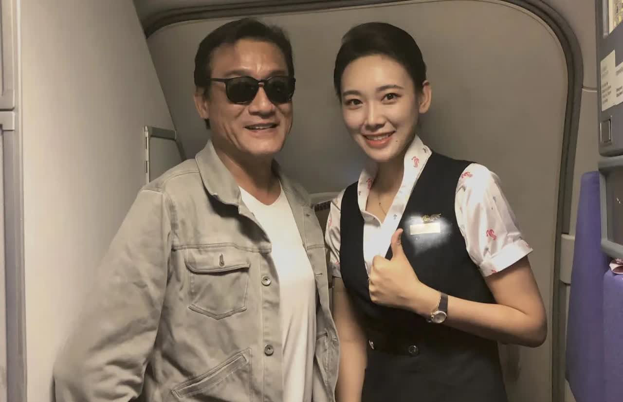 67岁梁家辉在飞机上和空姐合影，他的脸看起来很奇怪，下巴又长又歪，整张脸的五官很