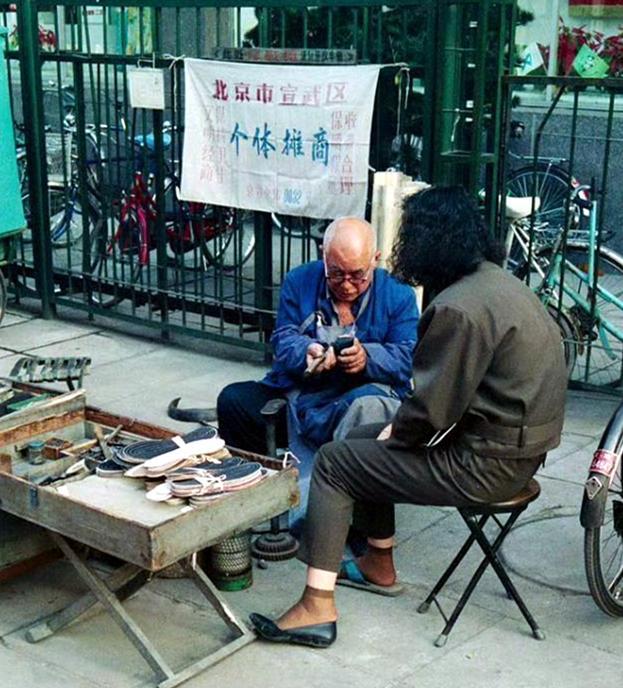 这是1900年北京宣武区一处个体修鞋摊。三十多年前，修鞋摊分布在城市的各个角落。