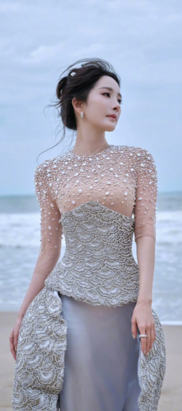 杨幂似从深海珍珠蚌中走出的缪斯，缀满珍珠的薄纱如海浪凝结的结晶，与银灰长裙在沙岸