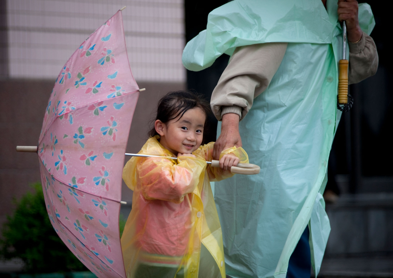 2012年平壤，身穿雨衣撑伞的妈妈，手里拉着个小孩。