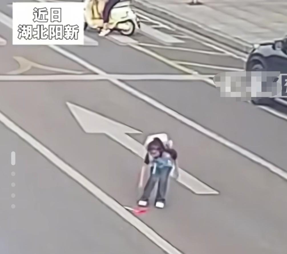 湖北阳新，车来车往的大街上，一位八九岁的小女孩突然走向马路中间，蹲下身捡东西，交