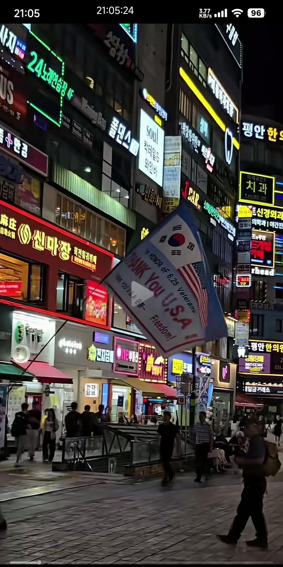 一个韩国人抗着一面旗帜在大街上游行
大大的美国国旗，小小的韩国国旗。
上面还用英