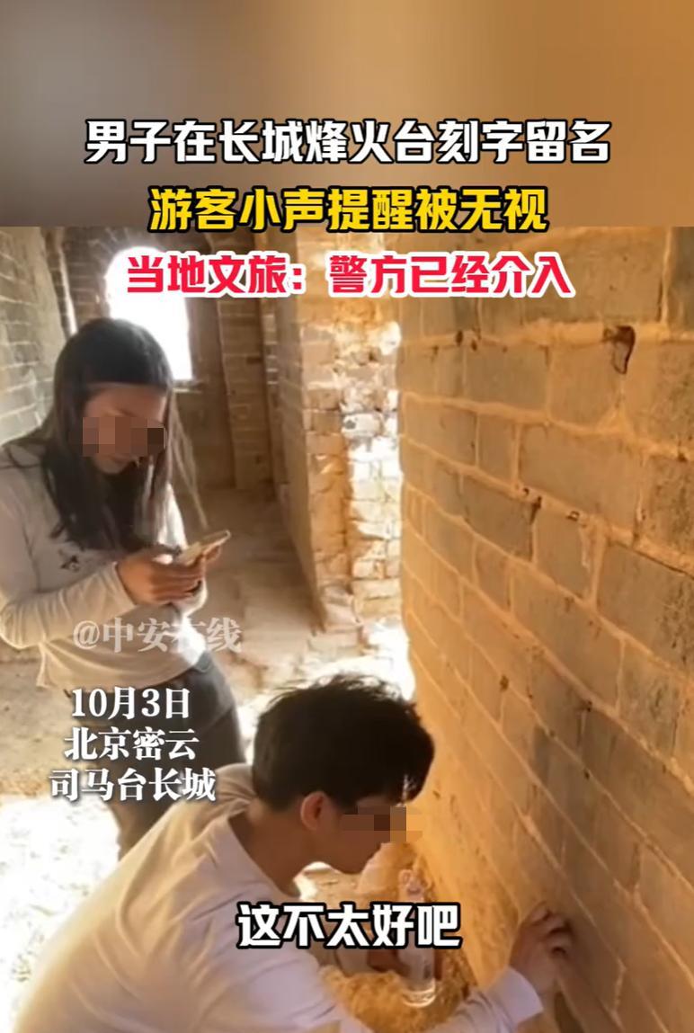 北京，在古老的司马台长城上，一名男游客用硬物在城砖上刻下名字和爱心，他的女同伴不