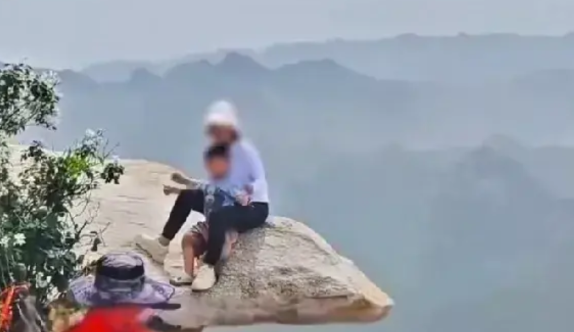 一名女游客带着自己的孩子在景区悬崖边拍照，而旁边拍摄者也不知道危险性，对着那名女