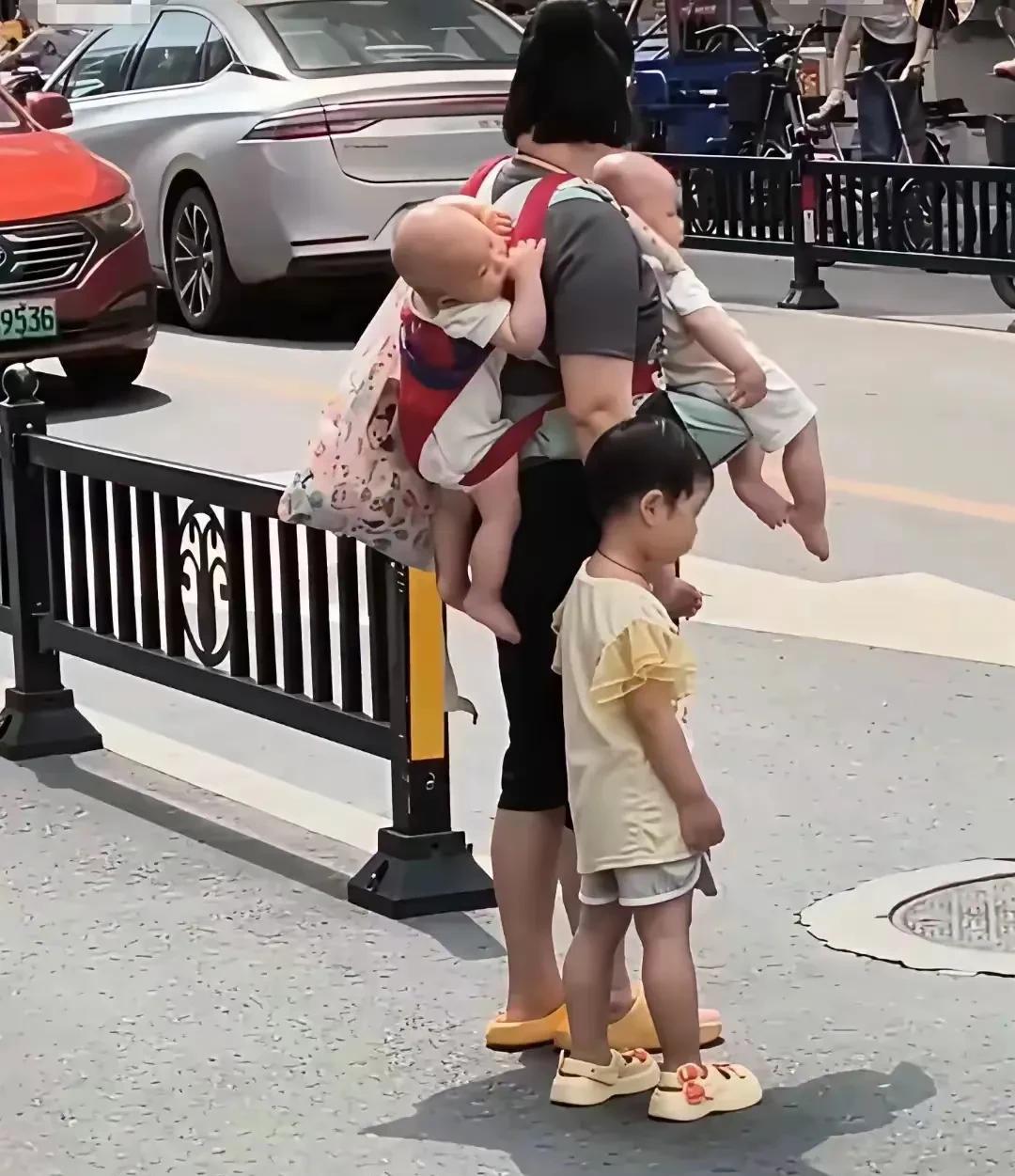 一个伟大无助的母亲，身上背着两个孩子，手里还领着一个孩子，这个当妈妈的真是太难了