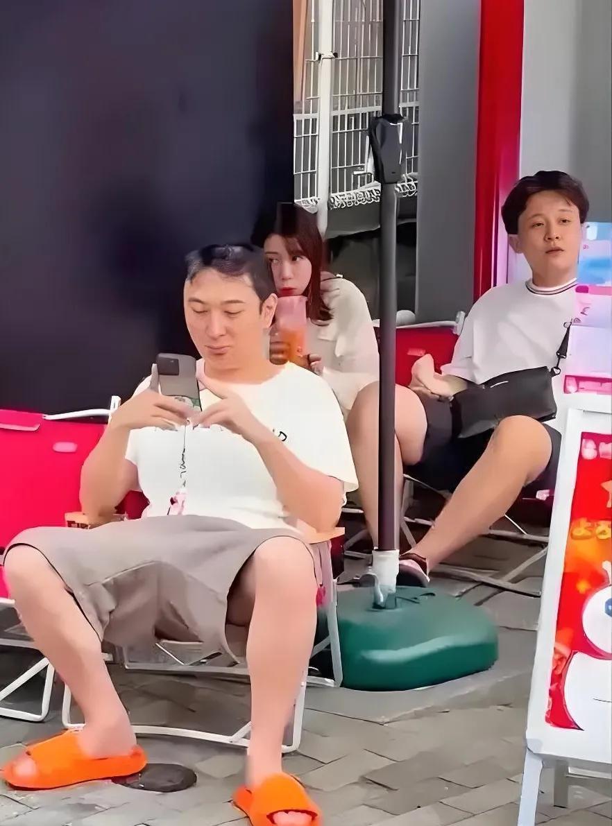 王思聪这样子还真看不出是富二代，他玩着手机，身穿白色短袖搭配大裤衩和拖鞋，他后座