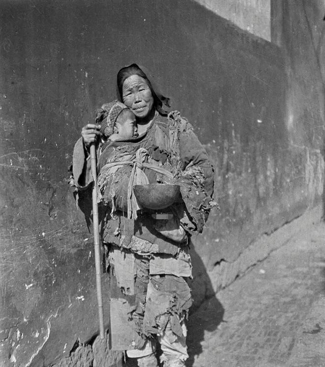 1919年，浙江杭州，一对沿街乞讨的母子的照片，镜头中母亲衣衫褴褛，手中拿着一个