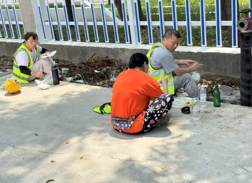 工地中午吃饭时间，工人坐在马路边吃着盒饭喝着啤酒，正好被路过的业主看到了，随即询