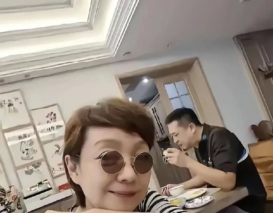 张嘉译在吃早餐
王海燕戴了个小墨镜
笑不滋的拍照，王海燕穿着一件很平常的条纹