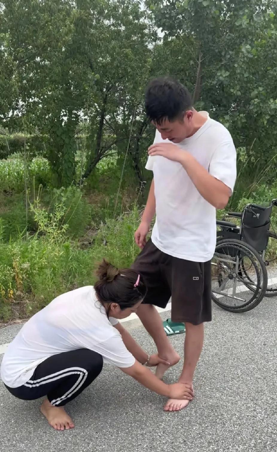 男人每吃力费劲地走一步后，蹲在地上的女人就用一只帮着男人，慢慢抬起另一只脚，路人