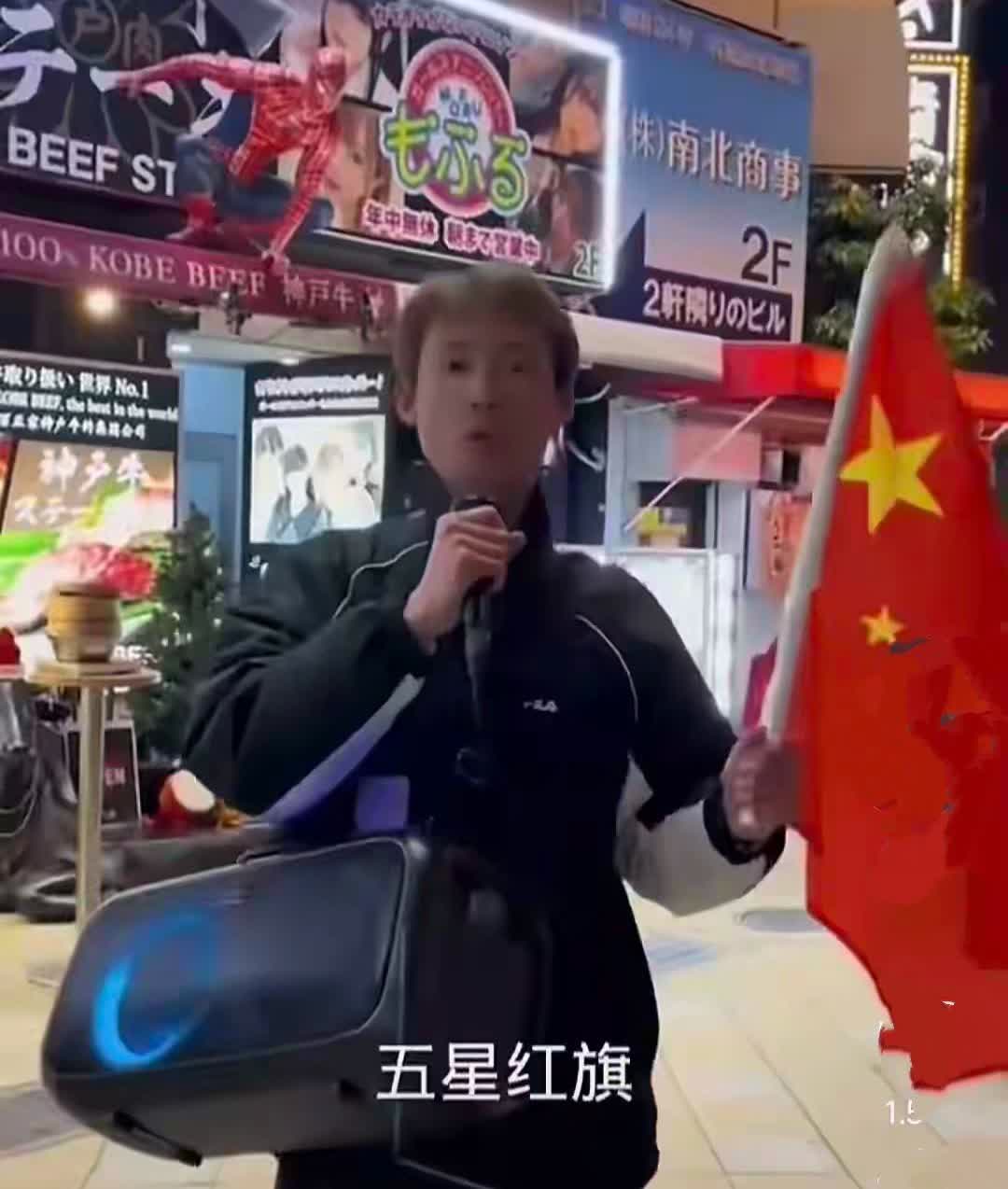 一个小伙子在日本挥舞着五星红旗，放声高唱《歌唱祖国》，而日本民众并未围观。
倘