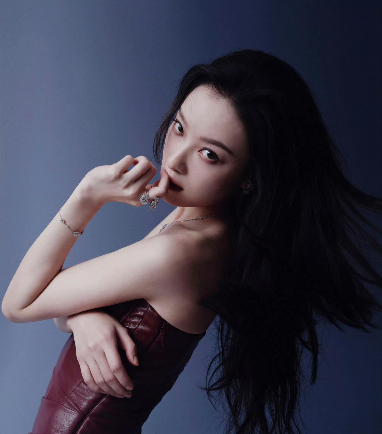倪妮身穿酒红色皮质抹胸裙，勾勒出曼妙曲线，珠宝点缀更显精致。发丝随风轻扬，每一个