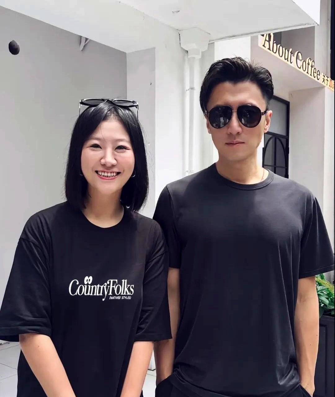 谢霆锋与饭馆老板娘的合影照，谢霆锋两手插兜，表情凝重。
身穿黑色体恤，身材壮实，