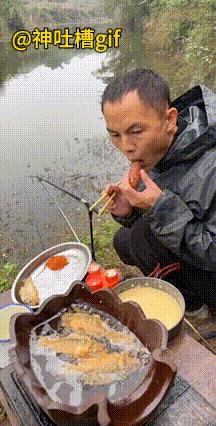 钓鱼人的午餐：河边搭着一口锅，锅里面正在油炸，男人边吃边钓鱼，忽然一条鱼上钩，简