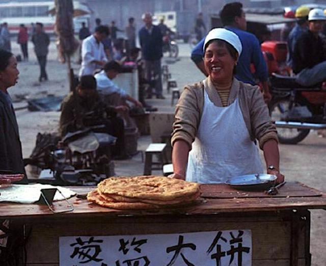 这是1990年代，贵阳的一位女摊贩在集市上摆摊卖葱盐大饼。她在集市小摊上现做现卖