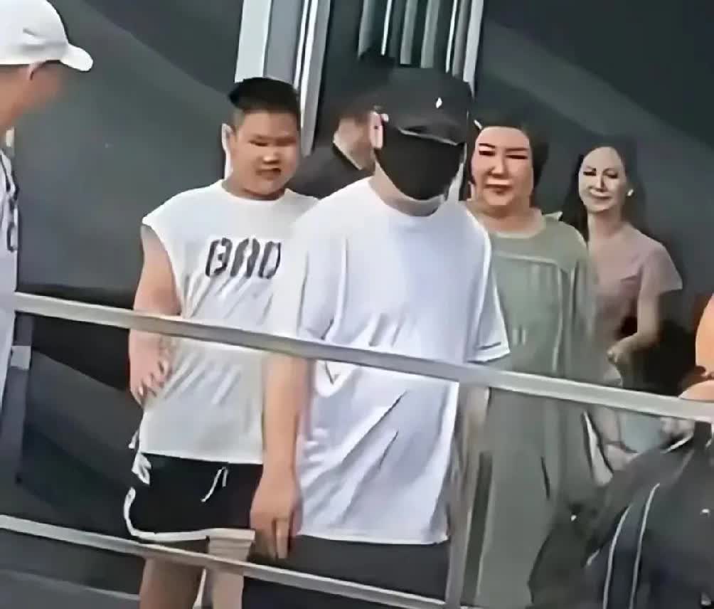 郭德纲携家人上海行，白汗衫蓝短裤穿戴很随意但脸蒙的太严实，妻子短发绿裙，手牵小儿