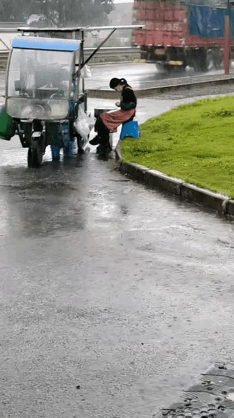 这位女士很勤劳，天下着雨，她还坚持摆摊，虽然不会有多少顾客。
这应该也是苦难，她