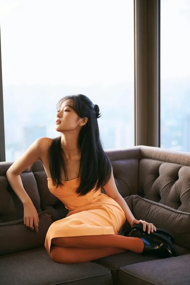 城市天际线作背景，她裹暖橘抹胸裙，长发或垂或绾，在沙发自在舒展