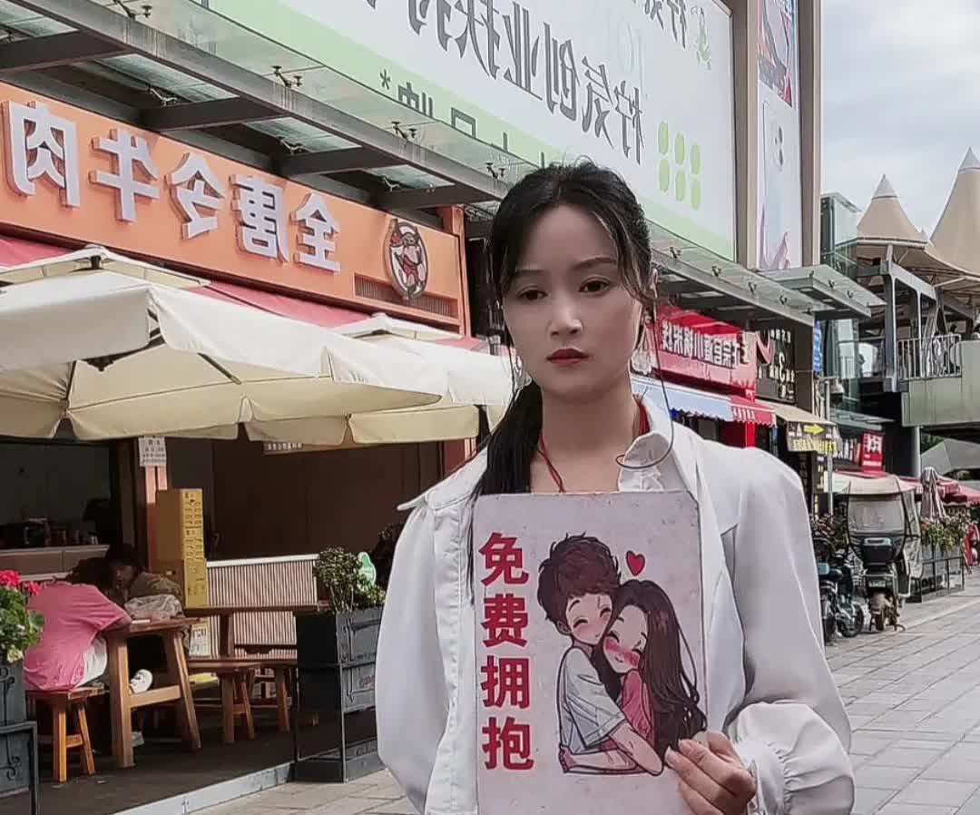 免费拥抱！？这个女孩举个牌子站在路边，目光呆滞，表情冷漠，这是演的哪一出？
一
