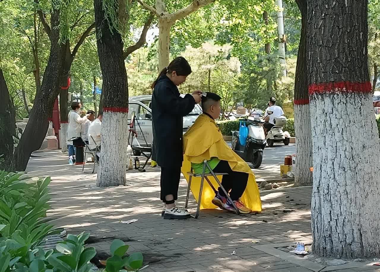 从前年开始，公园里就开始出现了低价理发的摊位。
今年，摊位越来越多，整个公园按