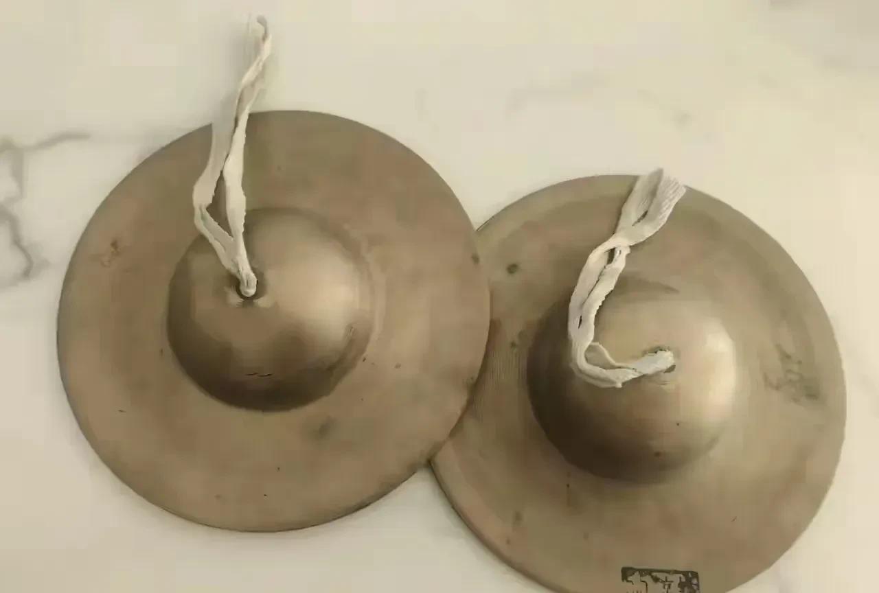 这两个圆圆的铜制物件，中间凸起，还系着白色布条。它们是乐器吗？可在哪些乐曲里会用