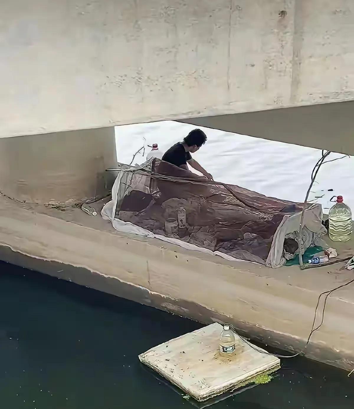 这哥们把用防蚊虫的门帘改个“帐篷”，就把桥底当成了家，吃喝拉撒全在这儿解决。说起