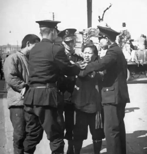 1948年，警员押解的落魄母子，围观者嬉笑。
旧社会