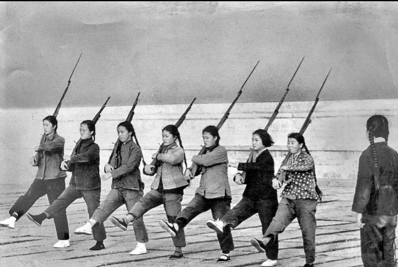 1966年，几位女民兵正在北京故宫旁边训练。
几个姑娘扛着步枪练习踢正步，表情严