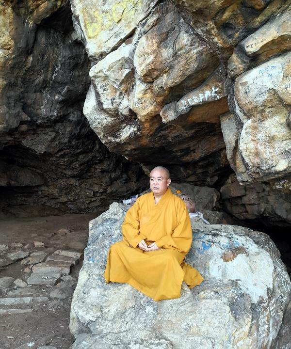 这是少林前住持释永信身穿僧衣在大石头上参禅打坐。释永信从小就与佛有缘。他的祖父母