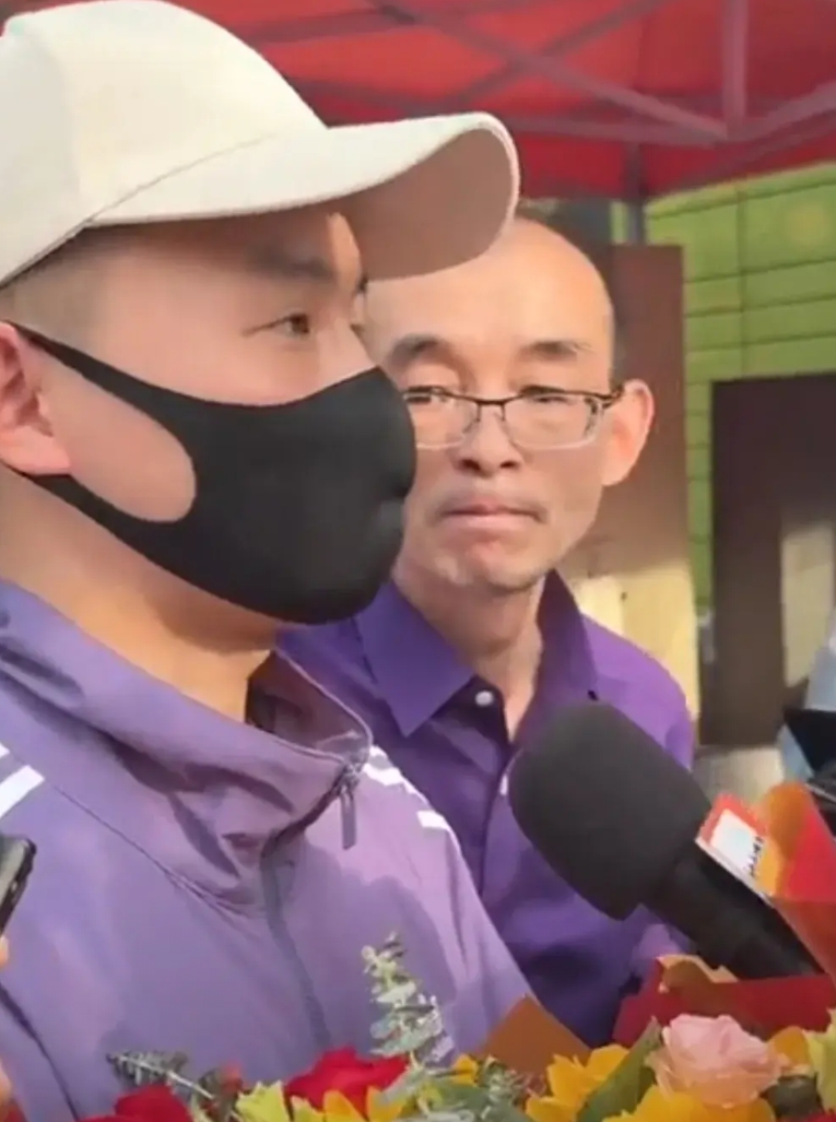 谢浩楠穿着紫色外套，黑色的裤子，白色鸭舌帽，黑色口罩。和爸爸一样，细长的眼睛。留