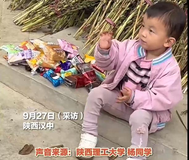 陕西，一位3岁小女孩坐在自家门口玩耍，这个时候看到一群来乡间拉练军训的大学生。小
