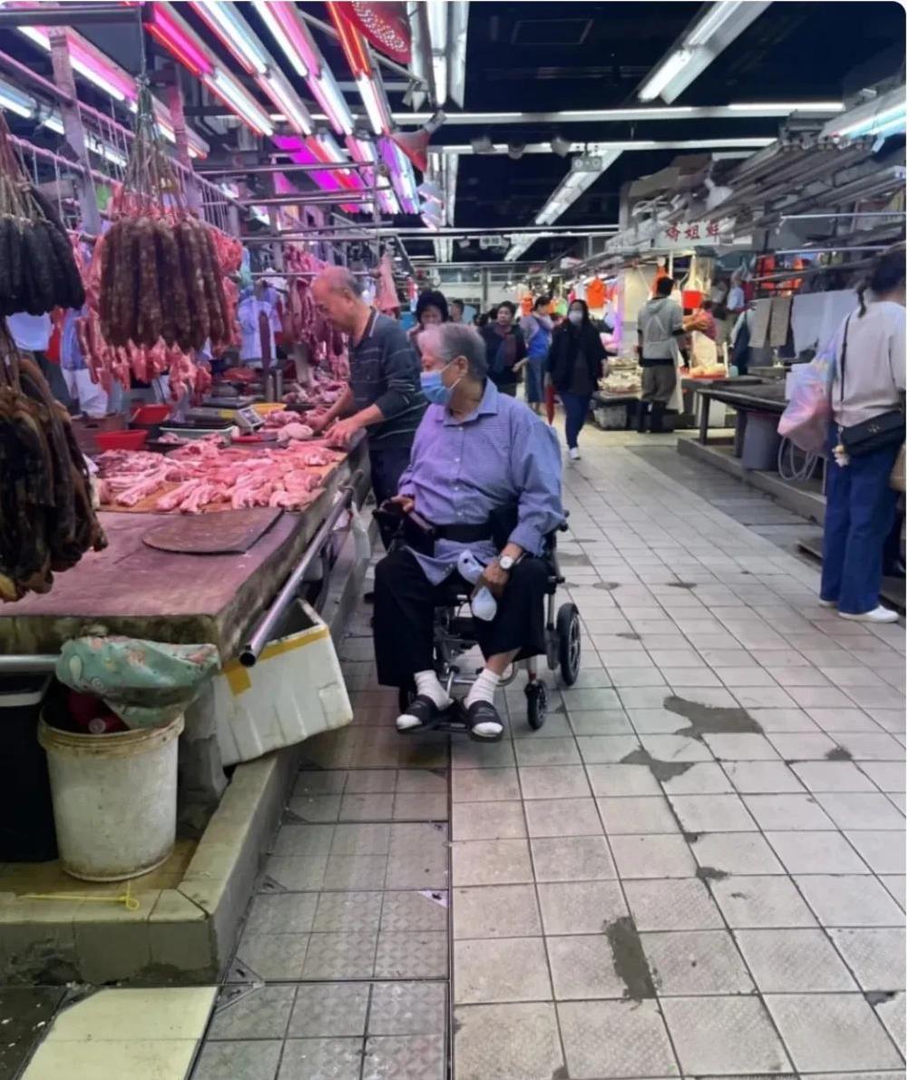 近日，著名功夫巨星洪金宝坐轮椅现身菜市场，头发花白，白袜子拖鞋，蓝色格子衬衫，这