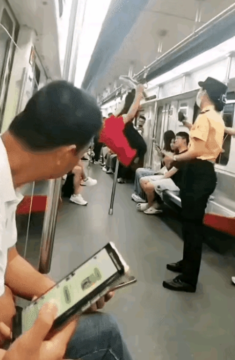 在地铁车厢内，一位身着红色 T 恤衫的老人，把车厢里的乘客扶杆当成了小区的单杠，