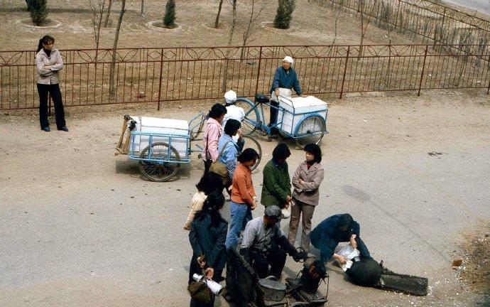 这是1983年沈阳街头摊主炸爆米花。爆米花摊位围满了人。她们都是排队等着炸自己的