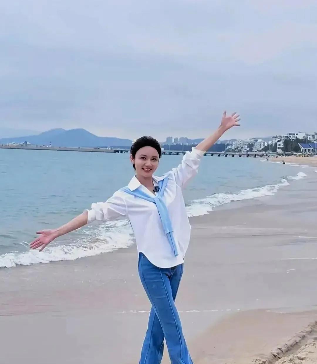 龙洋站在海边，海风吹乱了她的发丝，她张开双臂，仿佛要拥抱整个世界。