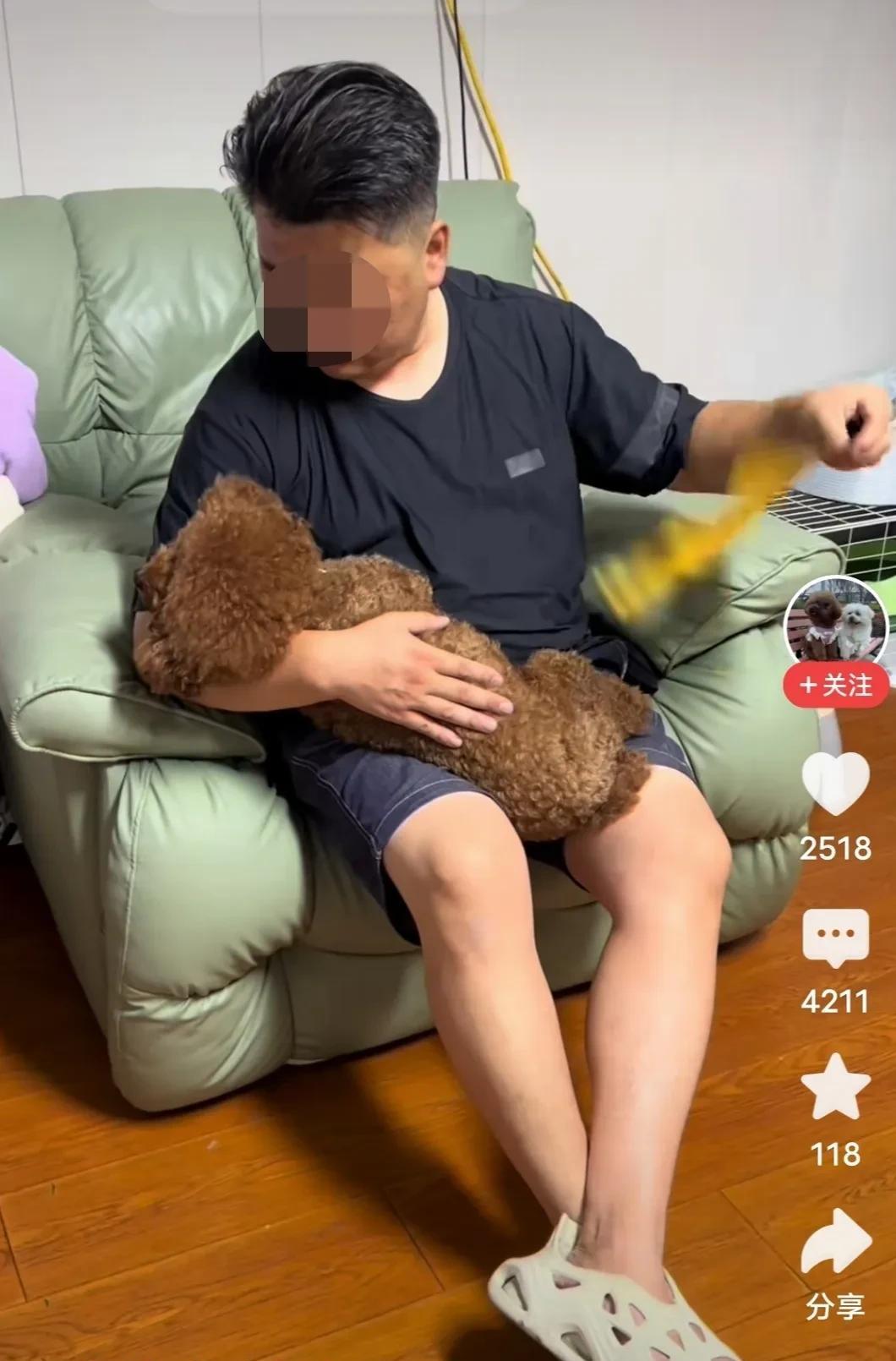 主人给小狗摇扇子，小狗依偎在男子怀里尽情的享受。反了，到底谁是主人啊？
男子坐在