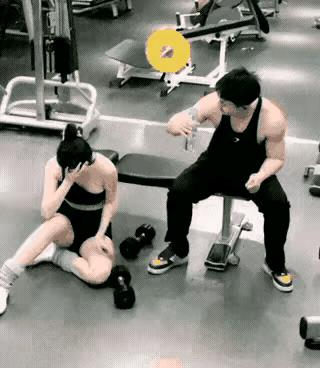 天上掉下个林妹妹。健身房内，女子拿着两个哑铃想躺在凳子上健身，一名男子拿着一瓶饮