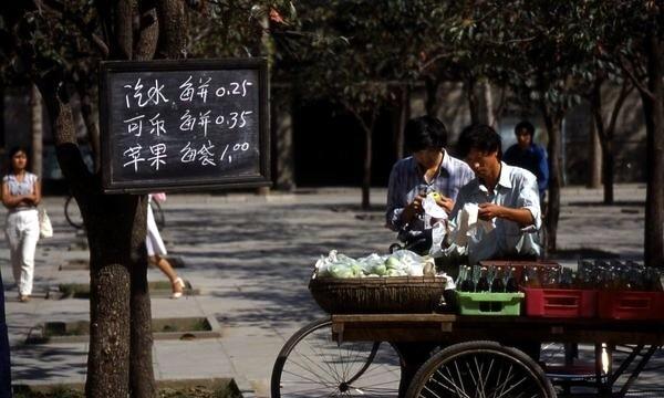1987年，两名青年人在摆摊。摊子上摆放着汽水、可乐与苹果。他们将每一种商品的价
